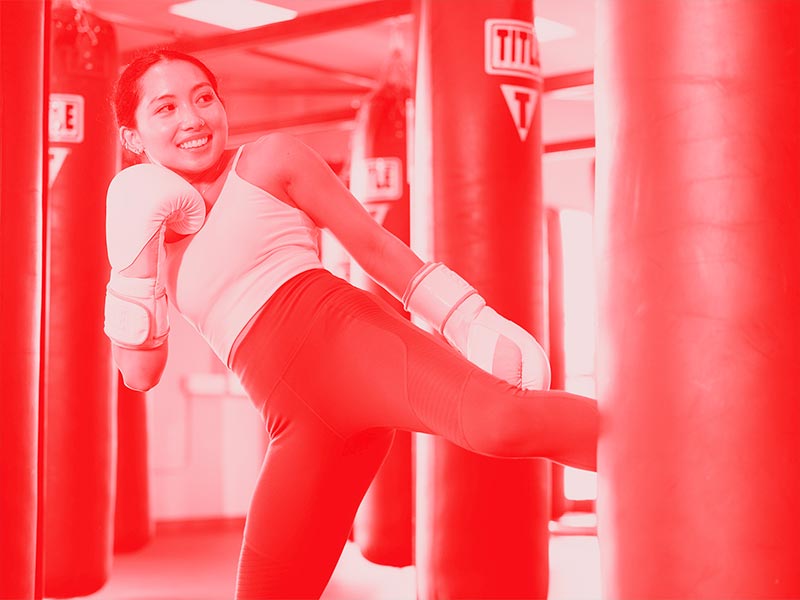 woman with gloves kicking heavy bag